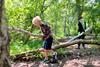 Two young boys carry a large branch in an area of woodland