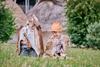 Two young boys wearing animal skin clothes sat on grass