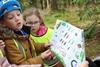 Young children on a school trip look at a bug identification map out in the woods