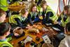 A group of kids in high-vis jackets gather round objects on a table