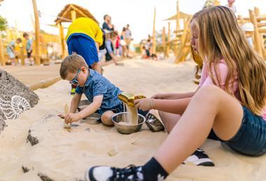 Two children dig in sand and brush fossils