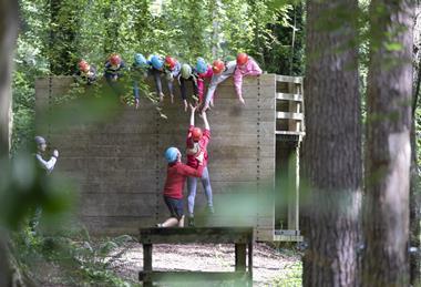A group of students help a teenage girl up on the low level ropes course at a Conway Centre residential