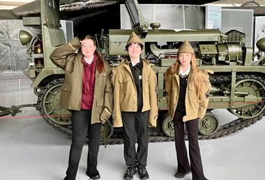 Three pupils stand in front of military vehicle while dressed in army clothing