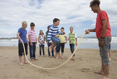 An instructor helps children skip over a rope on the beach