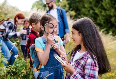 Students are seen looking through a magnifying glass and taking notes outside