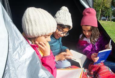 Three children in a tent reading books during a school camping trip
