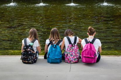 Girls with colorful Backpack Seated in front of Fountain