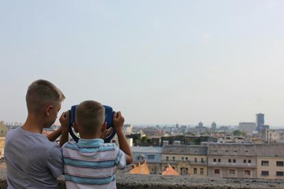 Two boys looking through a viewing projector in a city.