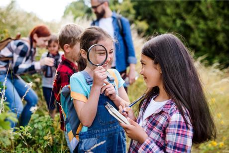 Students are seen looking through a magnifying glass and taking notes outside