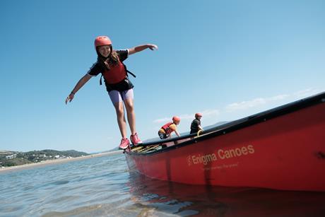 A girl balances on a canoe as part of an outdoor residential adventure with The Outward Bound Trust