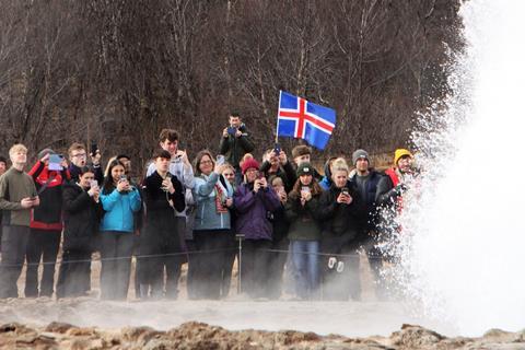 A group of students stand in awe watching Iceland's Great Geysir erupt.