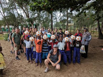 A group of children, students and staff holding footballs during an epedition to Kenya.