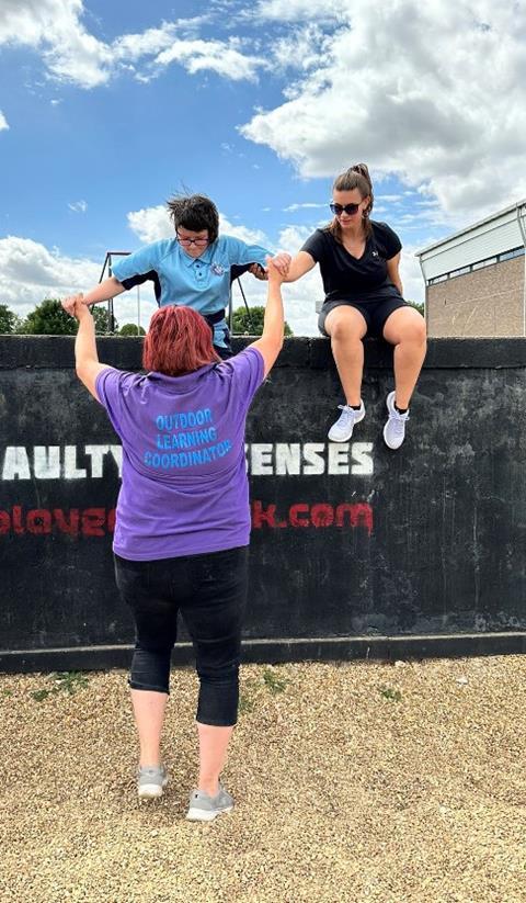 Becky Baldwin helping pupils over a climbing wall on a school trip