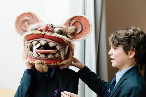 Two school boys trying on a wooden mask