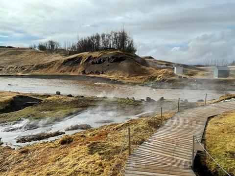 A view of the Secret Lagoon, Iceland with a walkway above the lagoon and steam from the springs.