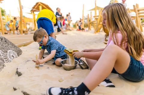 Two children dig in sand and brush fossils