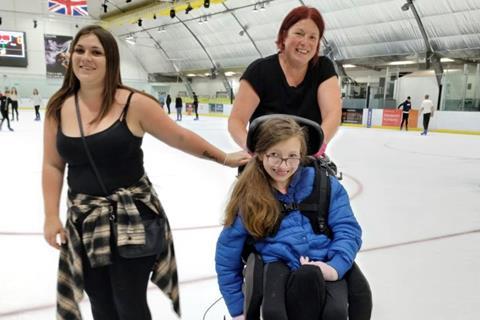 Becky Baldwin pushing a pupil in a whelchair on the ice while ice skating