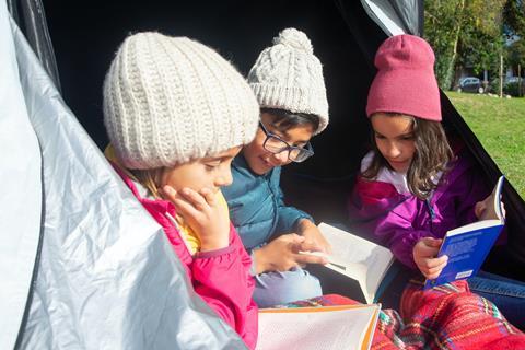 Three children in a tent reading books during a school camping trip