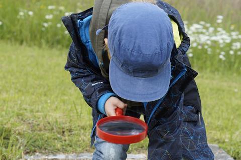 Young child looks through a magnifying glass on the floor