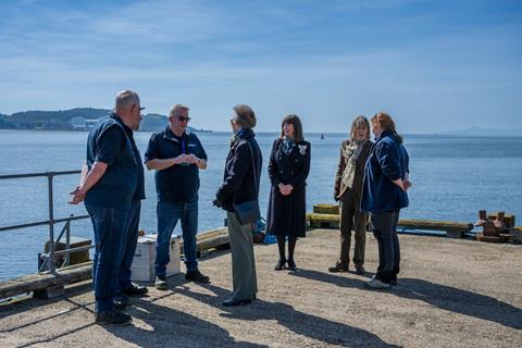 Princess Anne talks with a group of staff on a jetty over the sea.