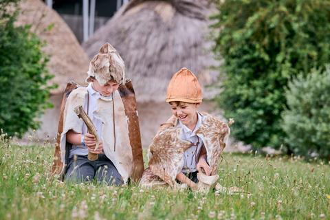 Two young boys wearing animal skin clothes sat on grass