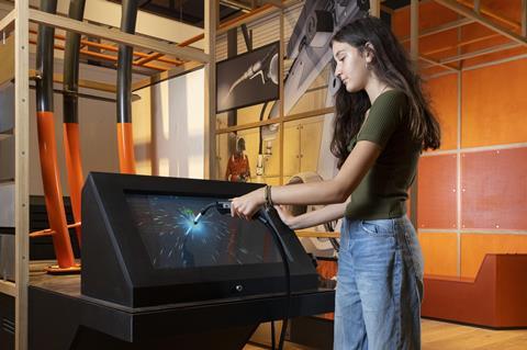 A teenage girl simulates welding in an interactive exhibit