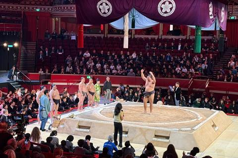 Sumo wrestler stands on stage with school children sat in the audience