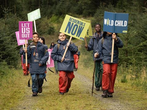 A group of young people hold banners and flags supporting the Let Us Out campaign to make outdoor residentials part of the school curriculum