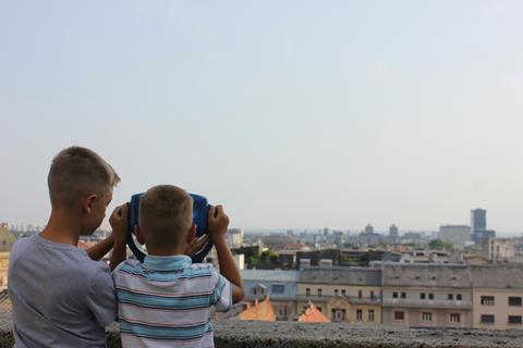 Two boys looking through a viewing projector in a city.