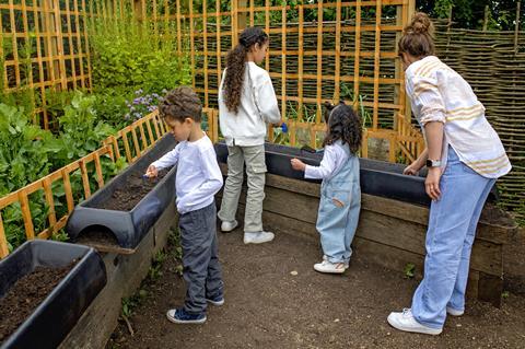 Three children and an adult woman dig through troughs of soil