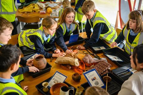 A group of kids in high-vis jackets gather round objects on a table