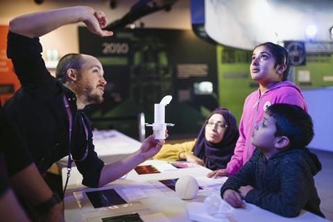 A member of staff at the Science Museum shows a woman and two children an experiment