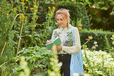 A teacher writes in her notebook surrounded by a beautiful green garden