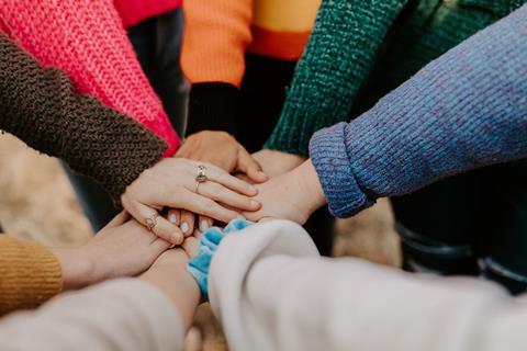 A group of people place their hands on top of each other to signify teamwork