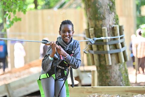 A young girl in a harness holds on to ropes at a Go Ape course