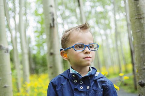 A young boy wearing a hearing aid in the woods